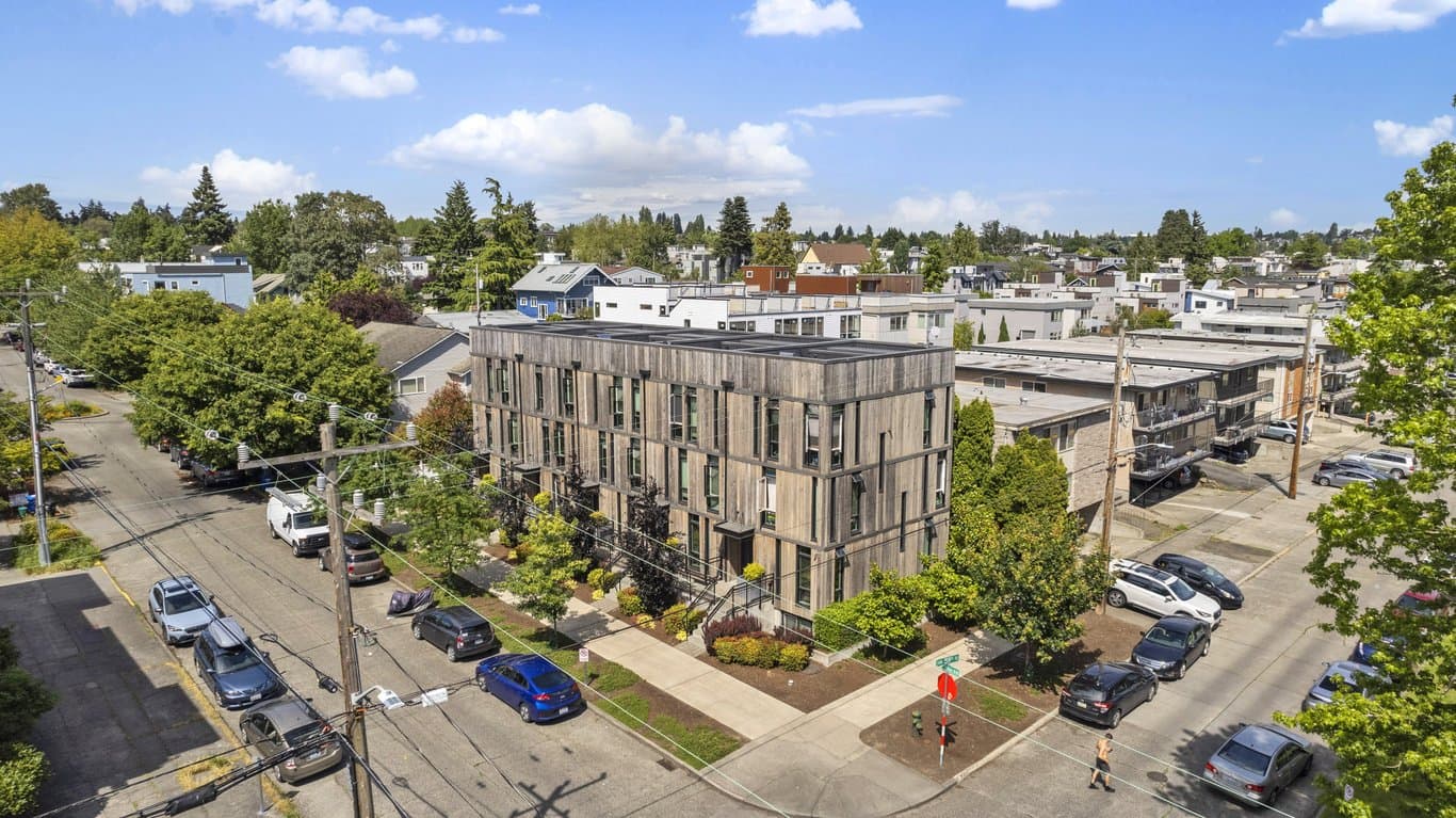 Aerial view of Pivot Apartments, a modern wood-sided building surrounded by streets, trees, and r...