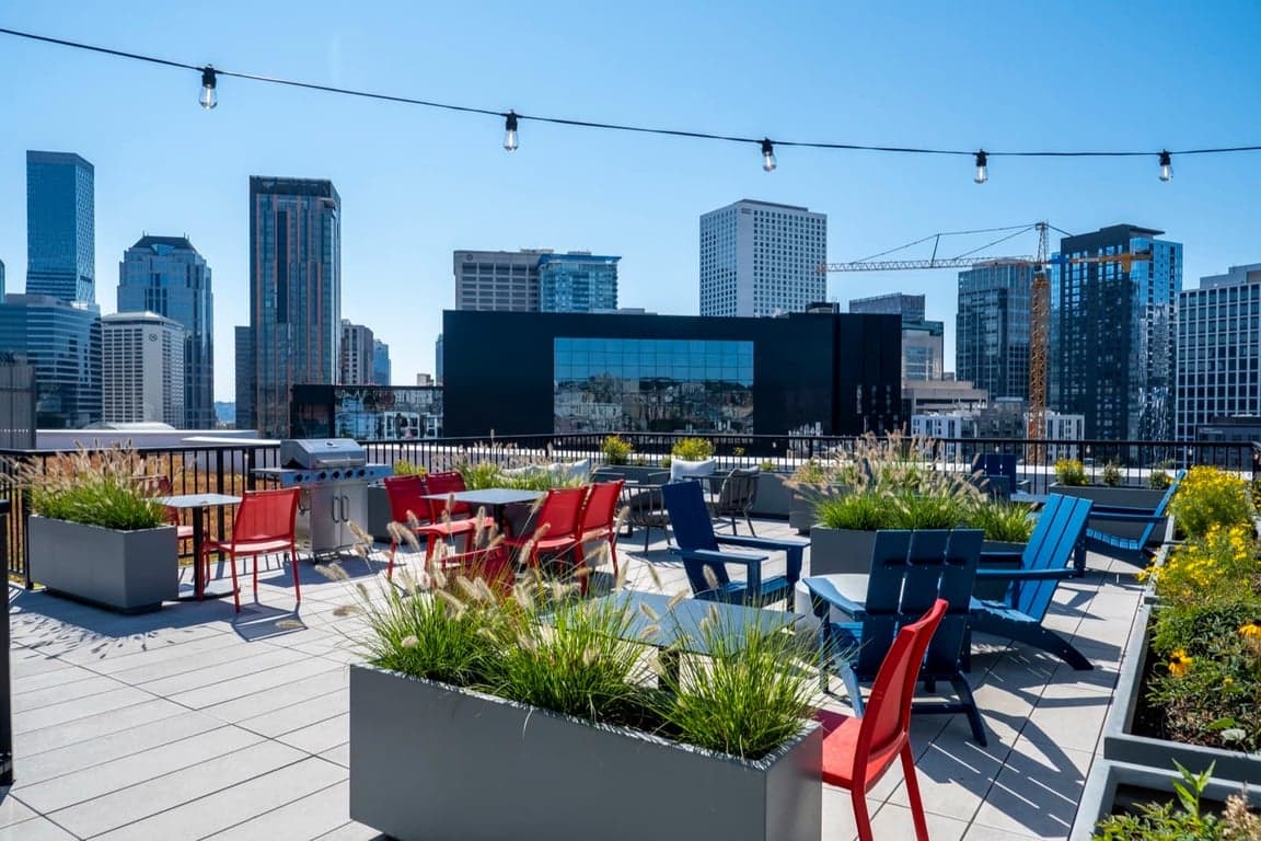 A rooftop patio with red and blue chairs and a city skyline in the background.